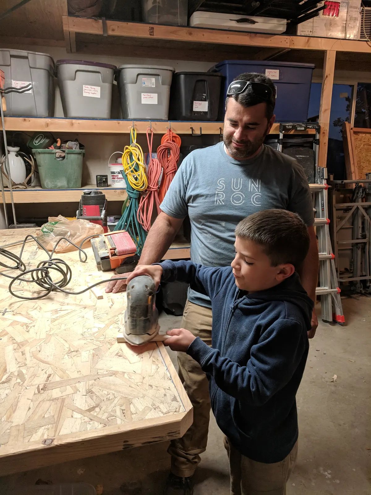 Levi Tippetts teaching his son to use a sander in the shop