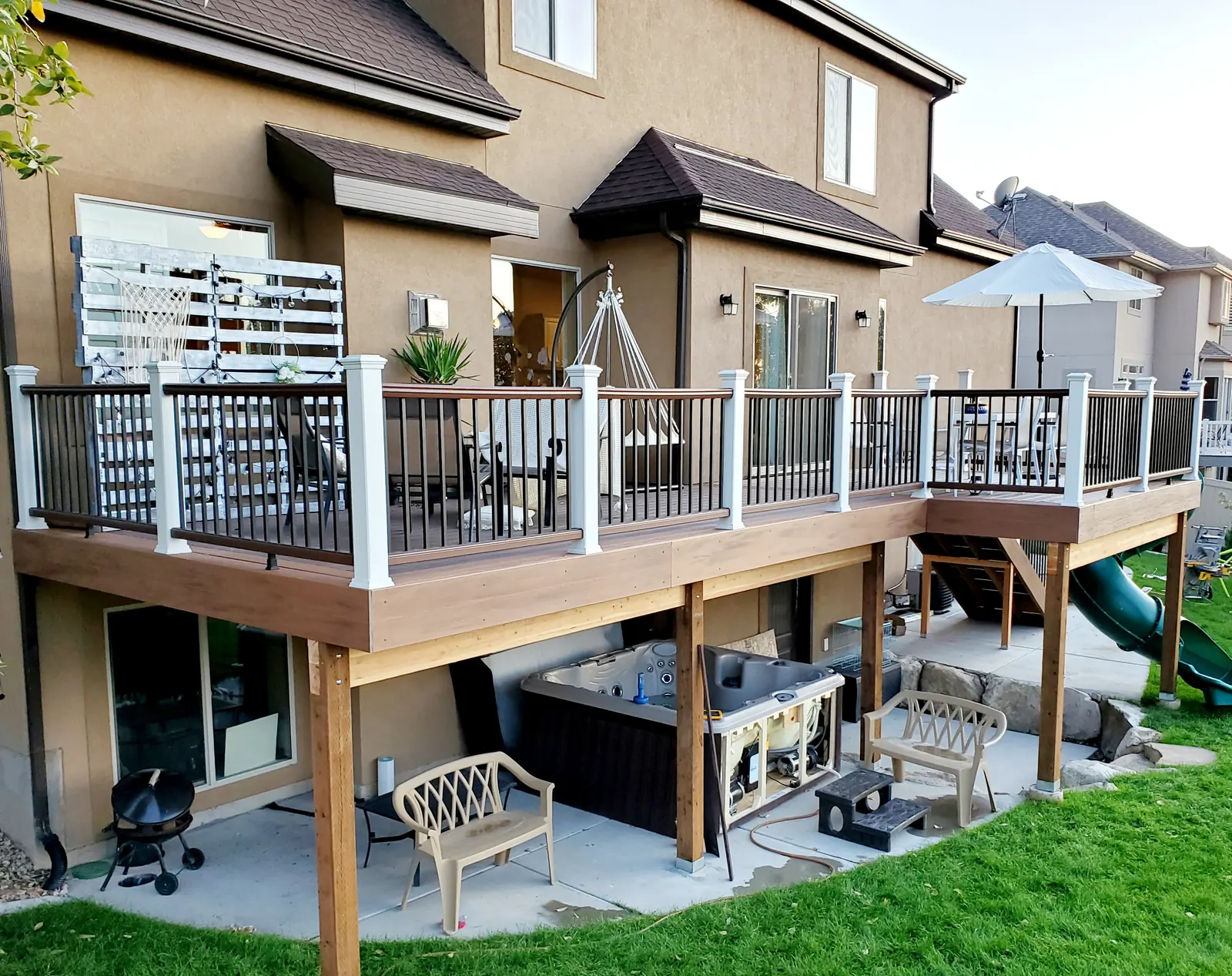 Second-story composite deck with white posts and black balusters over a covered patio