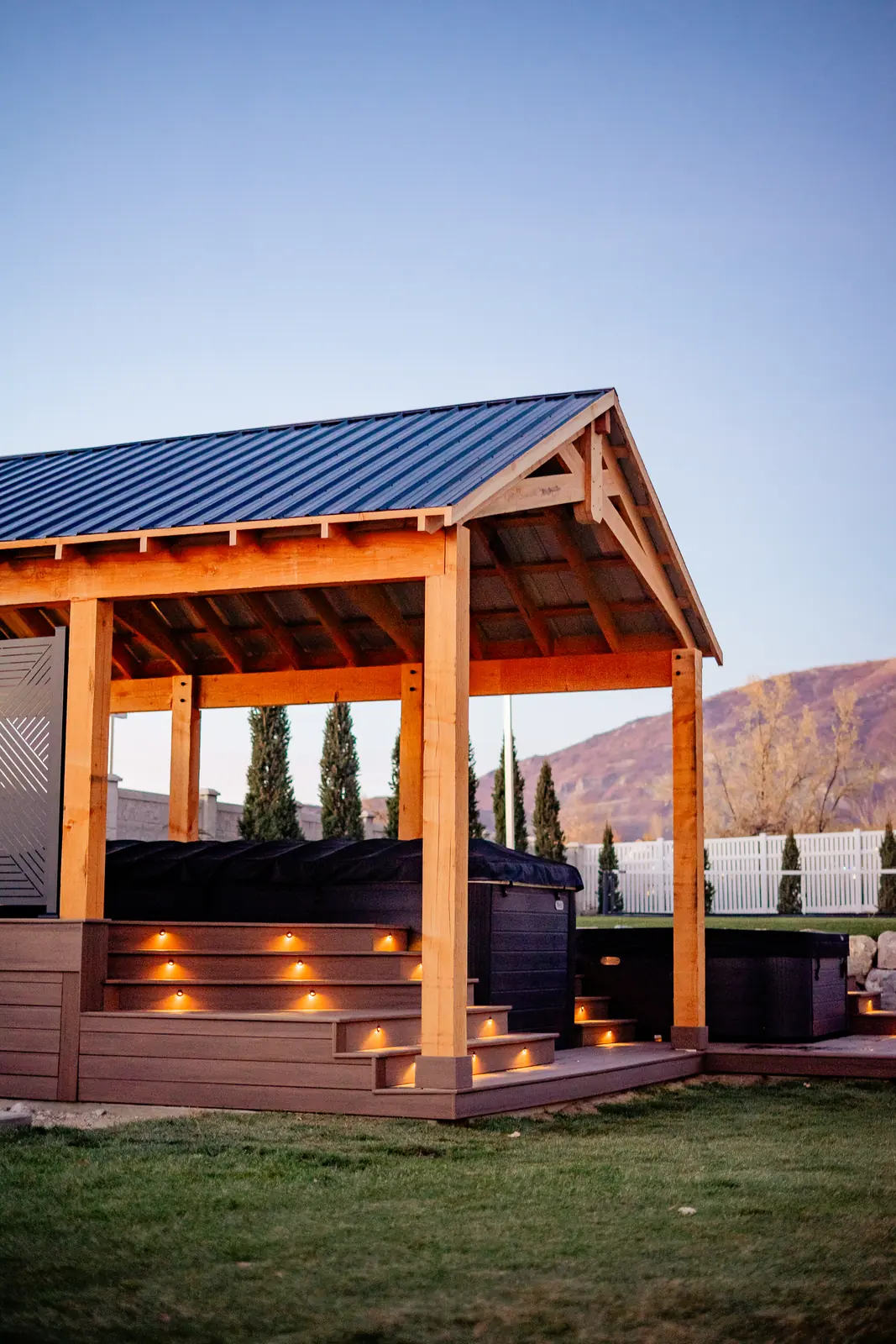 Rough-sawn timber pavilion with a metal roof over a hot tub deck with step lights