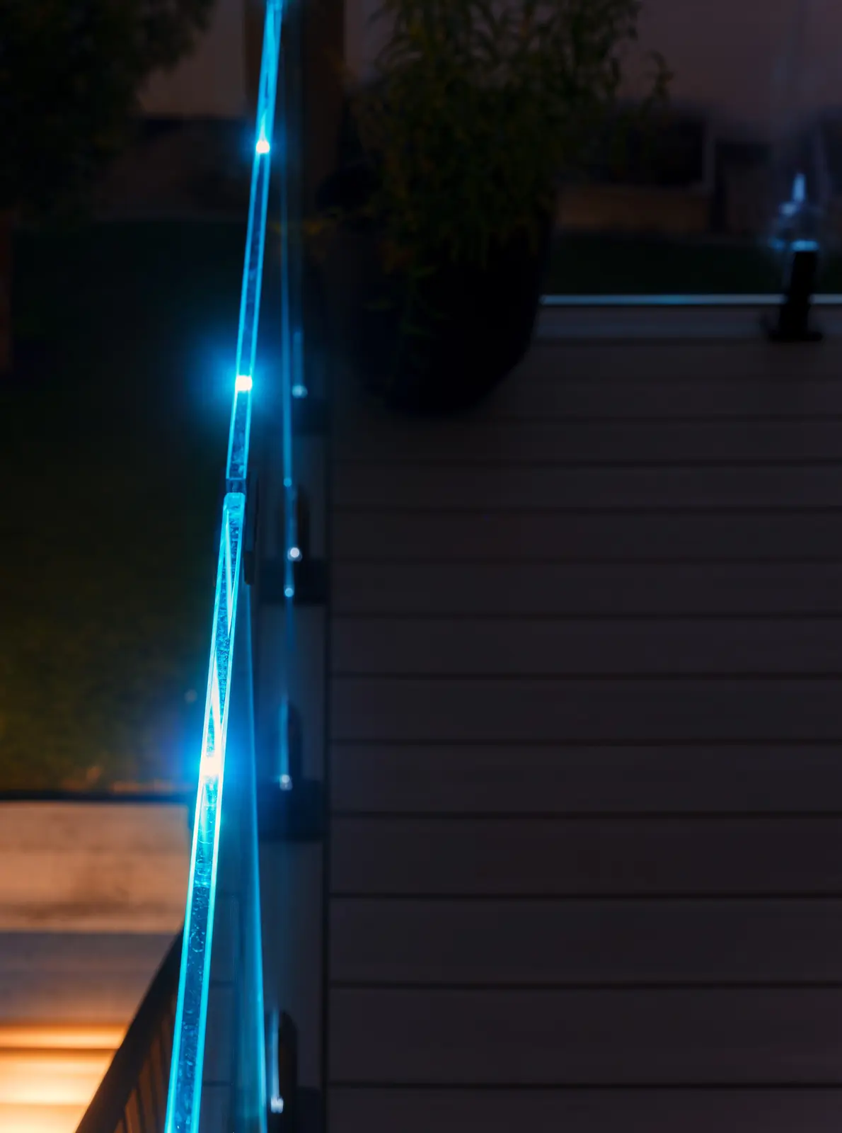 Blue-lit edge of an IG glass railing above lit deck stairs