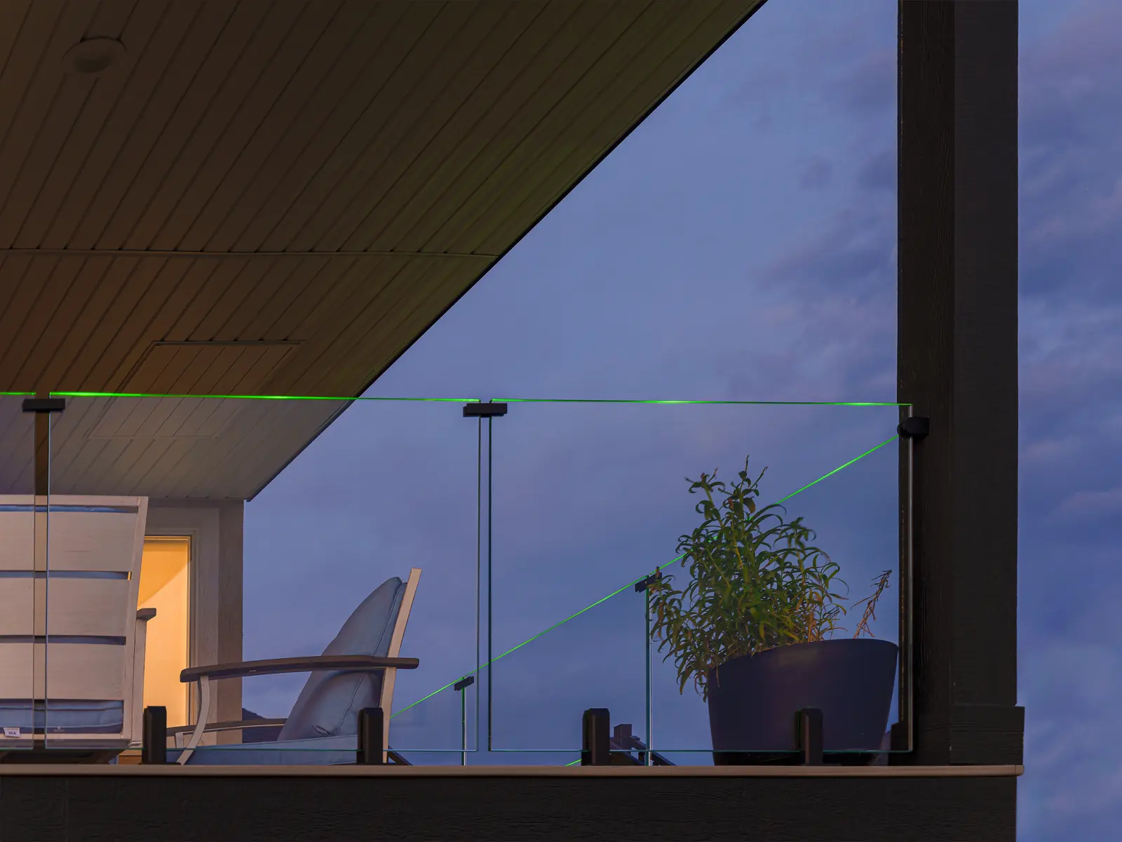 Illuminated frameless glass railing on a covered deck at dusk