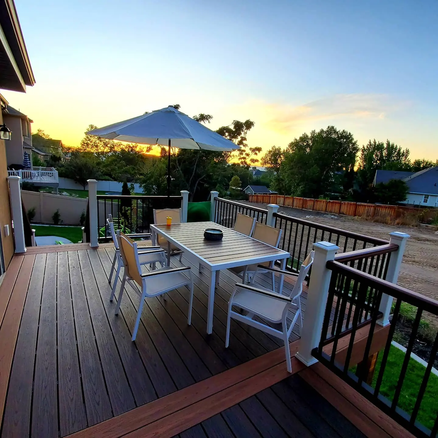 Two-tone Trex deck with a dining table and white and black railing at sunset