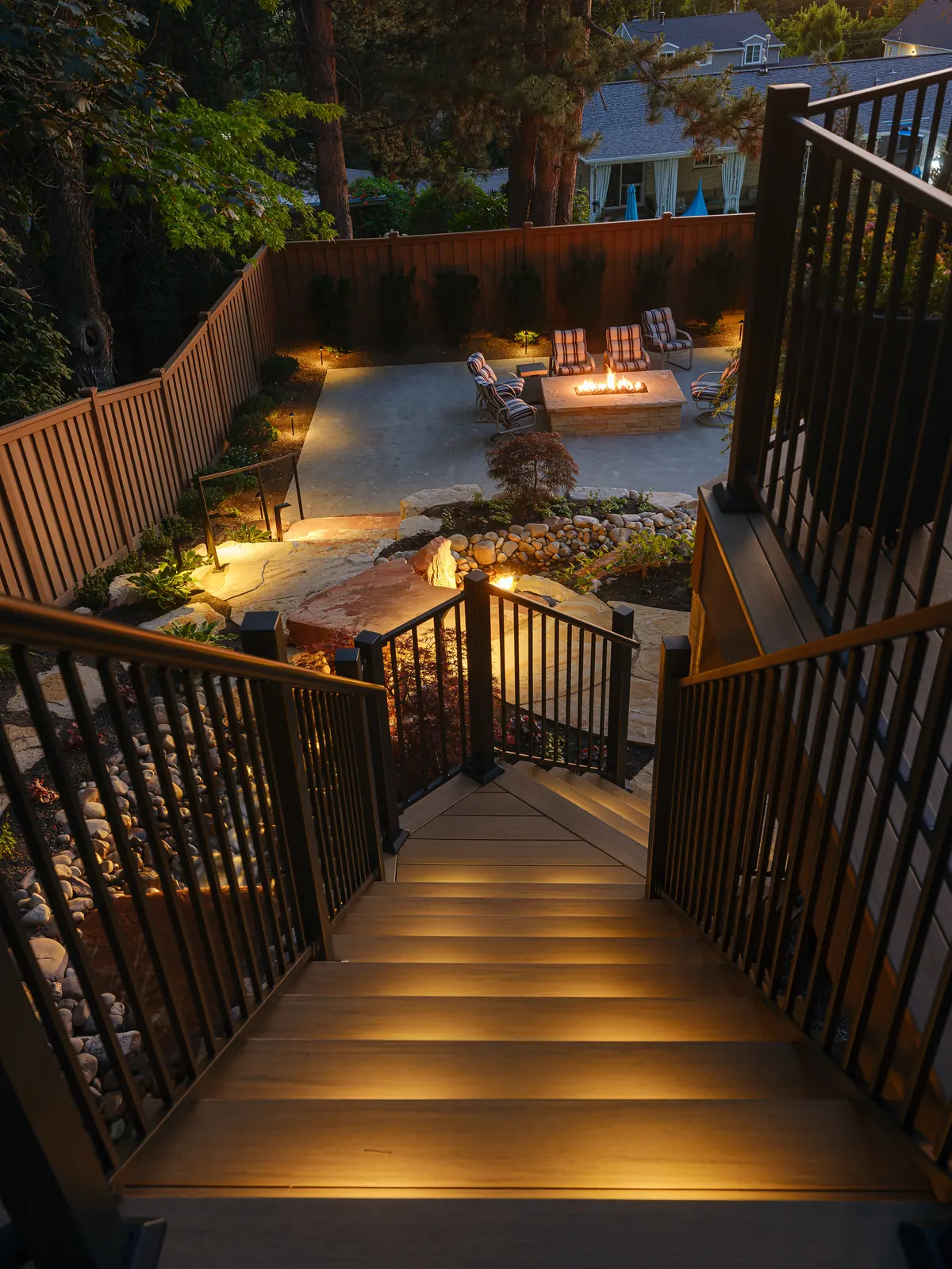 Lit deck stairs leading down to a backyard fire pit patio
